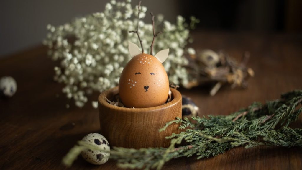 Charming Easter egg decorated with deer face, surrounded by natural elements on wooden table.