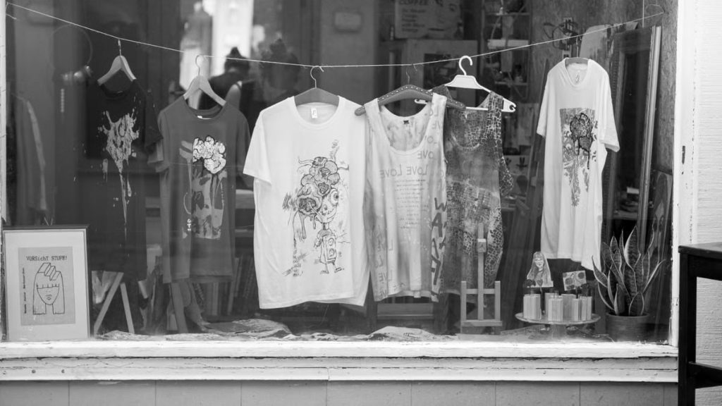 Monochrome window display featuring graphic t-shirts and merchandise in a retail store setting.